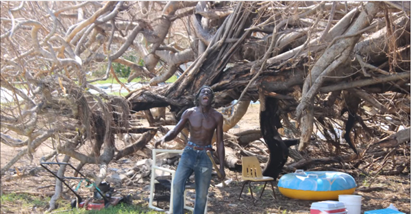 Man on Crooked Island standing in front of an uprooted tree following the passage of Hurricane Joaquin.