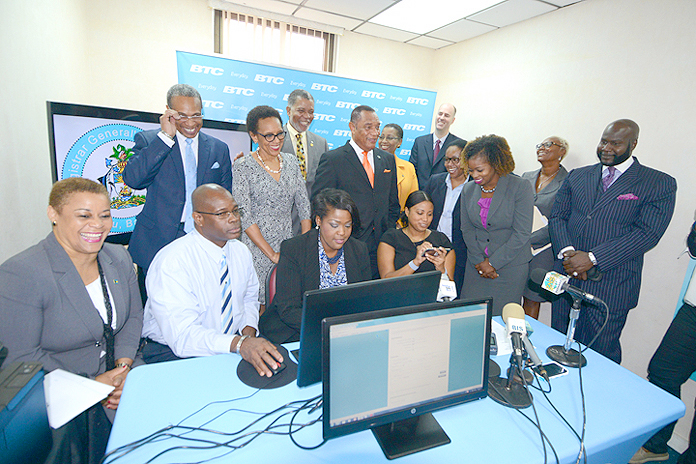 Incorporating companies online by computer, and smartphone at the E-Services Launch at Registrar General’s Department, January 5, 2016. Looking on are Prime Minister Perry Christie, standing centre right; Attorney General Allyson Maynard Gibson, standing centre left; and Minister of Financial Services Hope Strachan, seated left. (BIS Photo/Peter Ramsay)