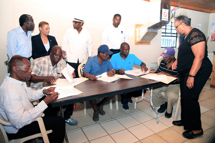 Melanie Roach of the National Repair and Reconstruction Unit oversees the signing of contracts awarded to contractors for repairs to Government buildings damaged during the passage of Hurricane Joaquin in October 2015. The contracts were signed Thursday, February 25, 2016. Pictured from left are contractors Julius Chisholm, Lionel Rolle, Curtis Hanna, Ivan Strachan and Marcel Collie-Moss. Standing from left are Harvey Roberts, Family Island Administrator, Acklins; the Hon. Hope Strachan, Minister of Financial Services, Investments and Local Government; the Hon. V. Alfred Gray, Minister of Agriculture and Marine Resource and MP for MICAL; and Captain Stephen Russell, Director, NEMA. (BIS Photo/Derek Smith)